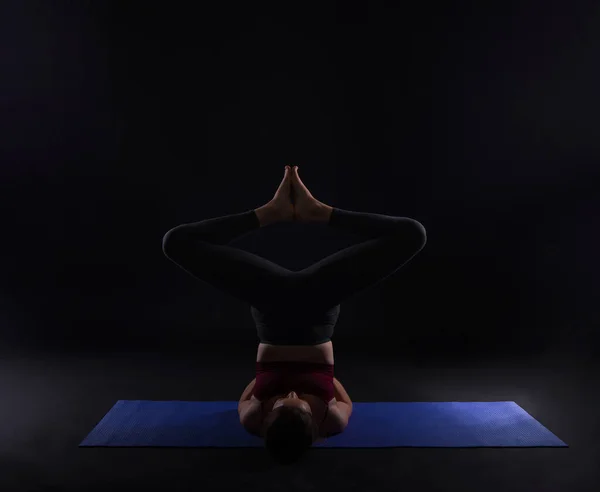 Jovem mulher do esporte fazendo ioga no tapete sobre fundo escuro — Fotografia de Stock