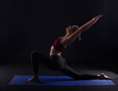 Genç sporcu kadın siyah arka planda yoga yapıyor.