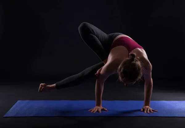 Молода спортивна жінка робить йогу на килимку на темному фоні — стокове фото