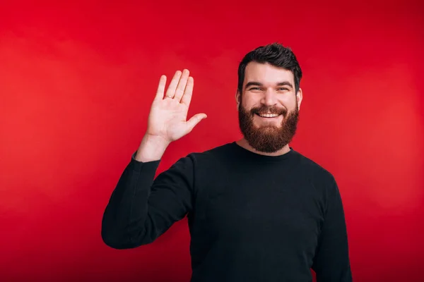 Fröhlicher bärtiger Mann grüßt, während er über rotem Hintergrund steht — Stockfoto