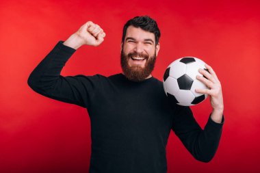 Mutlu genç adam zaferi kutluyor ve futbol topu tutuyor.