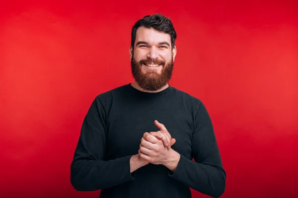 Schöner junger bärtiger Mann, der selbstbewusst in die Kamera blickt, die vor rotem Hintergrund steht — Stockfoto