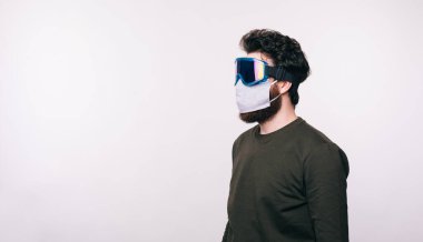 Beyaz arka planda duran yüz maskeli bir adamın yan görüntüsü.