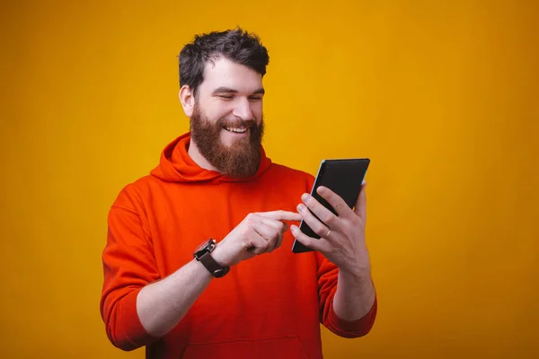 Smiling bearded man is typing something on his tablet on yellow background. — Stock Photo, Image