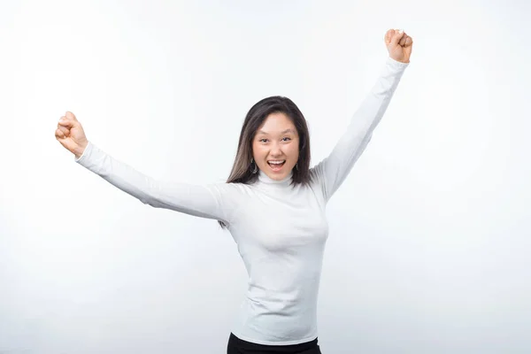 Amazed young woman celebrating success with arms up over white background — Stock Photo, Image