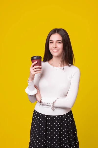 Caucásica estudiante femenina está sonriendo a la cámara mientras sostiene una taza para llevar . — Foto de Stock