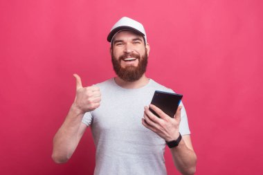 Şaşırmış sakallı adam baş parmak işareti yapıyor ve tablet tutuyor.