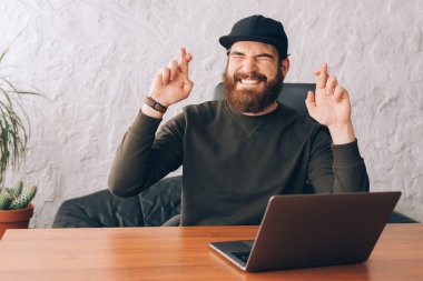 Genç sakallı adam ofiste oturuyor ve şans diliyor ve hayal kuruyor.