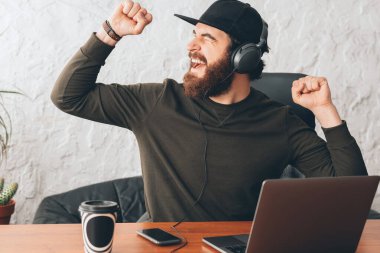 Ofisteki neşeli genç adam kulaklıklarda müzik dinliyor ve dans ediyor.