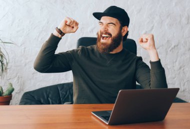 Neşeli sakallı hippi adam ofiste sızlanıyor ve zaferi kutluyor.