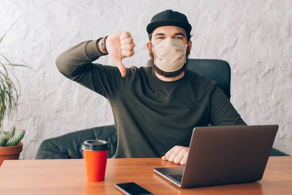 Trabalhador de escritório homem de pé na frente do laptop com máscara anti vírus e mostrando polegares para baixo — Fotografia de Stock