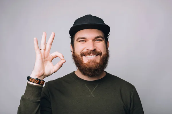 Fröhlicher bärtiger Hipster-Mann zeigt OK-Geste über weiße Wand — Stockfoto
