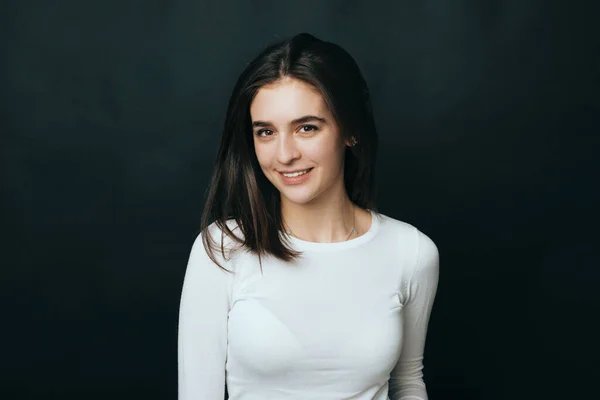 Joven mujer alegre sonriendo y mirando con confianza a la cámara sobre fondo negro en el estudio — Foto de Stock