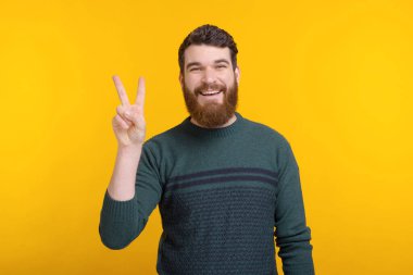 Neşeli genç adam sarı arka planda barışçıl bir jest gösteriyor.