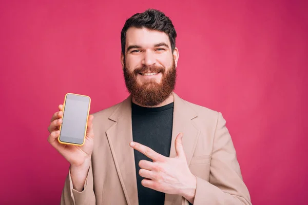 Feliz hombre sonriente en traje apuntando a teléfono inteligente sobre fondo rosa — Foto de Stock