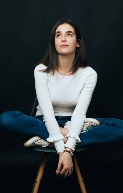 Kelebek pozisyonunda oturan genç ve güzel bir kadın bir sandalyede durup yukarı bakıyor..