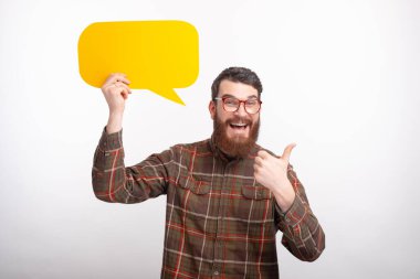 Neşeli erkek öğrenci başparmağını kaldırıyor ve beyaz arka planda sarı baloncuk konuşması yapıyor..