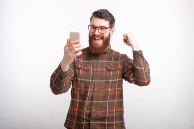 Telefonuna bakan genç adam beyaz arka planda kazanan hareketi yapıyor..