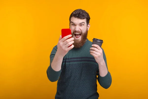 Homem barbudo segurando um copo de papel preto está gritando em seu telefone . — Fotografia de Stock