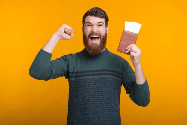 Young bearded man has won a trip for two is makeing winner gesture while holding a passport and tickets. — Stock Photo, Image