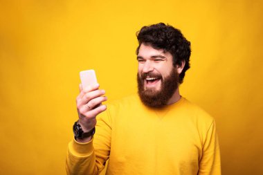 Gülümseyen adam telefonuna bakıyor sevdikleriyle internette konuşuyor ve mesafeyi koruyor..