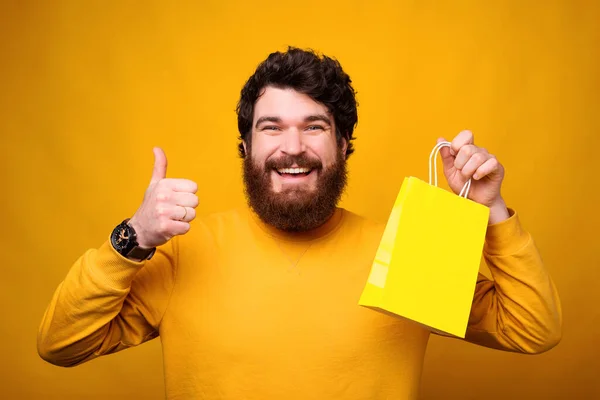 Ich schätze die Möglichkeit zum Online-Shopping. Lächelnder Mann zeigt Daumen hoch und gelbe Papiertüte. — Stockfoto