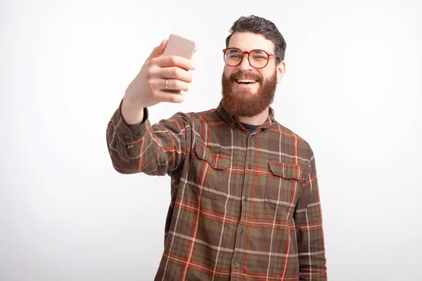 Joyeux jeune homme fait un selfie avec son téléphone sur fond blanc . — Photo