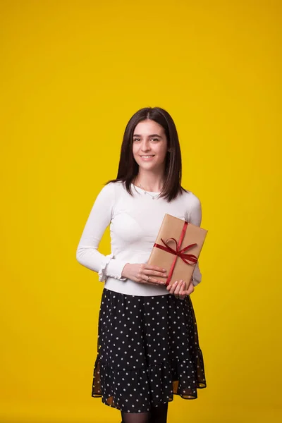 Foto vertical de una chica de pie presentando un regalo en sus manos . — Foto de Stock