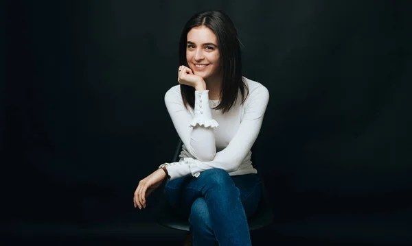 Retrato de una chica sonriente sentada en una silla sobre fondo negro . — Foto de Stock