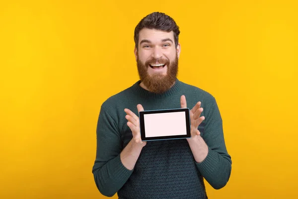 Hombre alegre está sonriendo a la cámara y mostrando la pantalla de su tableta . — Foto de Stock