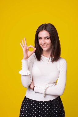 Neşeli genç bayan sarı arka planda dururken iyi bir jest yapıyor..