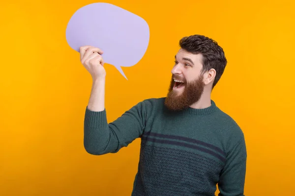 Sorprendido y emocionado hombre barbudo está sosteniendo un discurso de burbuja sobre el fondo amarillo . —  Fotos de Stock