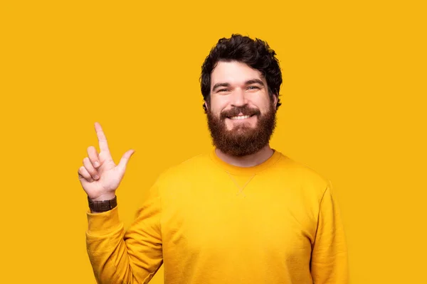 Hombre alegre está apuntando hacia arriba mientras sonríe a la cámara en el fondo amarillo . — Foto de Stock