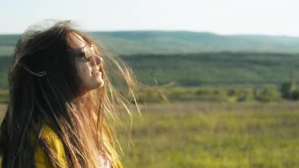 Dışarıda rüzgarlı bir günde gülümseyen güneş gözlüğü takan güzel genç bir kadın. — Stok video