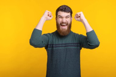 Sakallı adam sarı arka planda kazanan jesti yapıyor..