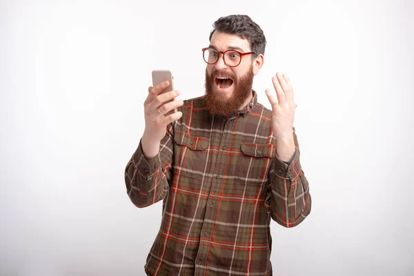 Surpreendido homem barbudo está olhando para seu telefone sobre branco . — Fotografia de Stock