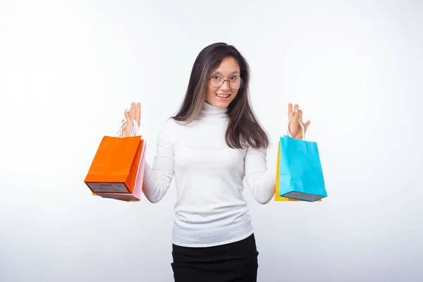 Веселая молодая женщина в очках держит несколько пакетов для покупок на белом . — стоковое фото