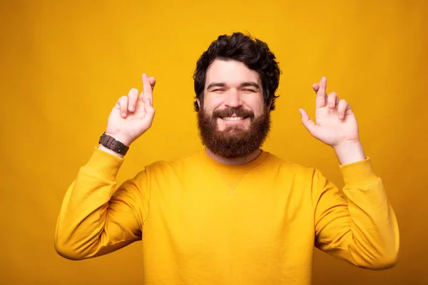 Augurando l'uomo barbuto sta facendo il gesto di speranza chiudendo gli occhi e incrociando le dita sul giallo . — Foto Stock
