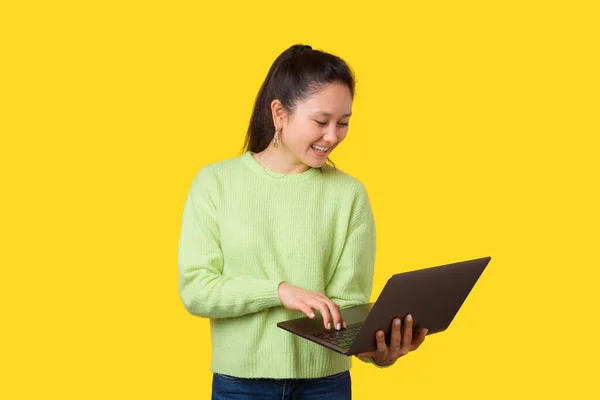 Giovane donna sorridente sta utilizzando un computer portatile o navigare in Internet mentre in piedi sopra giallo . — Foto Stock