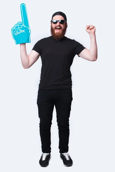 Foto de cuerpo entero barbudo hombre hipster con gafas de sol y apuntando con un gran guante de abanico sobre blanco —  Fotos de Stock