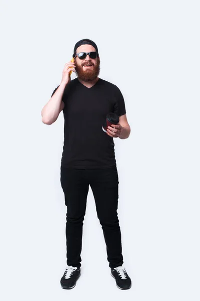 Full length photo of man with beard talking on phone and holding coffee — Stock Photo, Image
