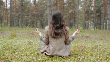 Ormanda oturan ve yoga yapan bir kadın.