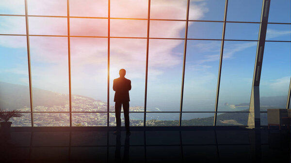 A male silhouette in a business suit on the background of an office pan-window overlooking coastal landscape.