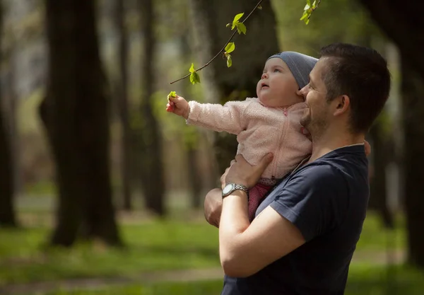 Mutlu bir aile. Baba kızın kollarında tutar. Bahar ağaçlar arka plan.