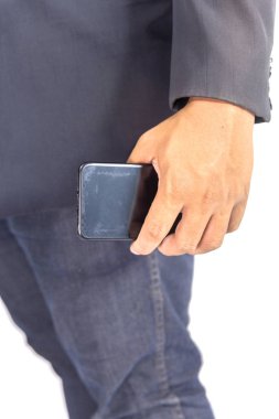 Takım elbiseli ve kot pantolonlu bir adam ayakta telefonu tutuyor.