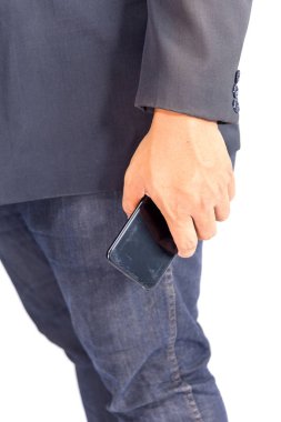 Takım elbiseli ve kot pantolonlu bir adam ayakta telefonu tutuyor.