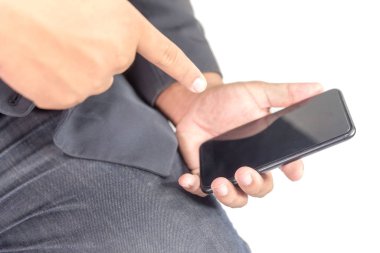 Takım elbiseli ve kot pantolonlu bir adam otururken telefonu tutuyor.