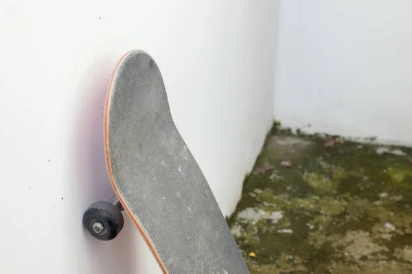 Skate encostado contra parede de concreto branco e chão sujo — Fotografia de Stock