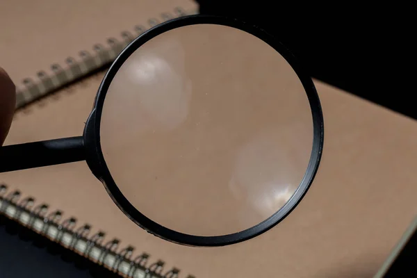Magnifying glass and notebook on black background, investigate c — Stock Photo, Image