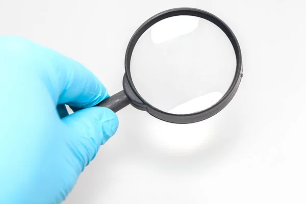 Hand in blue glove and magnifying glass — Stock Photo, Image